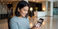 現代的なホテルのロビーで、スマートフォンを手に取り笑顔で見ているアジア系の若い女性。