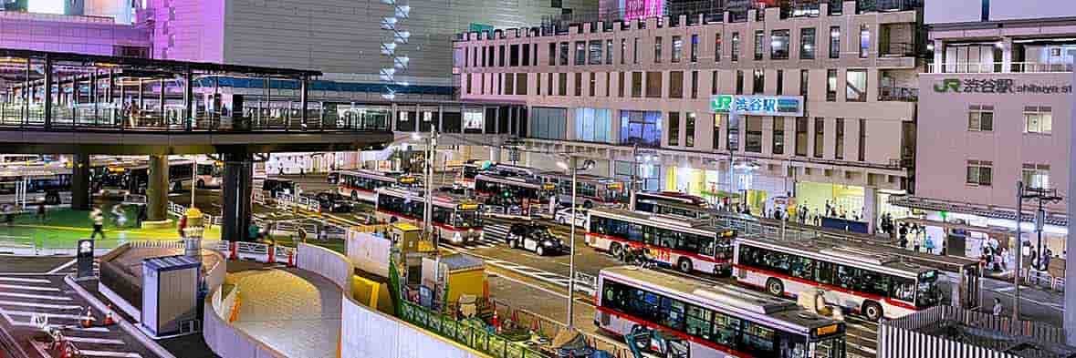 東京の主要ターミナル、渋谷駅前の夜景。バス乗り場には行き交う人々が見られる。