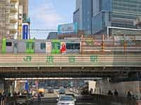 JR渋谷駅の大きな高架橋を電車が通過する様子。高架下には車道と人々が見える。