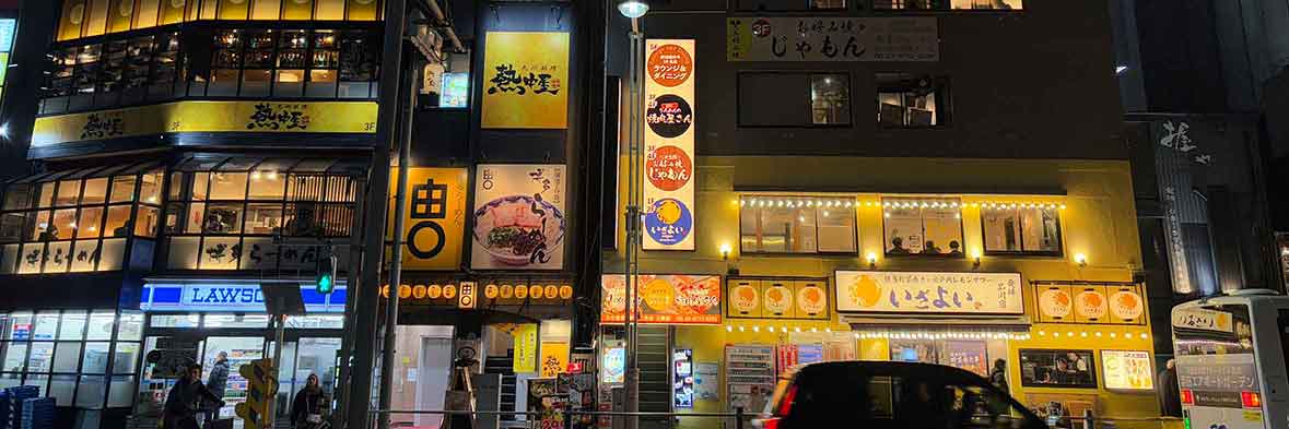 煌々と明かりが灯る品川駅東側のビル群。様々な店舗の広告が目に飛び込み、活気ある商業エリアの夜景。