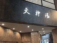 夜の住宅街に佇む「天神湯」の建物。シンプルなデザインの壁面に白い文字が浮かび上がっている。