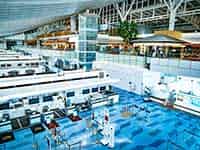 羽田空港の明るく近代的なターミナル内部。上階にはレストランやショップがあり、人々が行き交う様子。